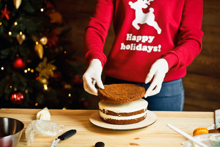 A girl in a Christmas red sweater at home prepares a cake for a festive table for a family holidayの写真素材