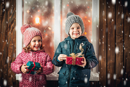On Christmas night an adorable little boy  with his sister a girl with gifts in hand near the window the snow falls. They are waiting for Santa Claus.の写真素材
