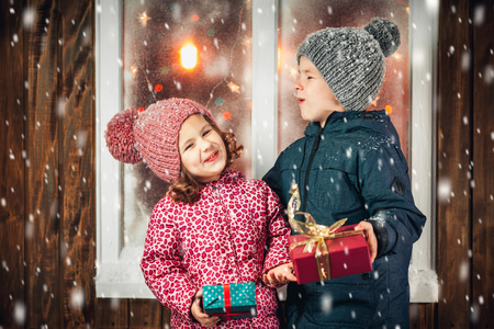 On Christmas night an adorable little boy  with his sister a girl with gifts in hand near the window the snow falls. They are waiting for Santa Claus.の写真素材