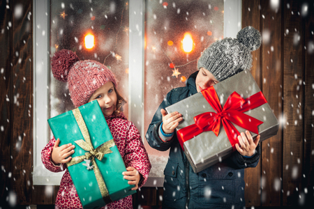 On Christmas night an adorable little boy  with his sister a girl with gifts in hand near the window the snow falls. They are waiting for Santa Claus.の写真素材