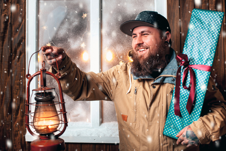 Christmas night, snow falling, funny man with a beard and with gifts in hand and flashlight at the window. Winter backgroundの写真素材