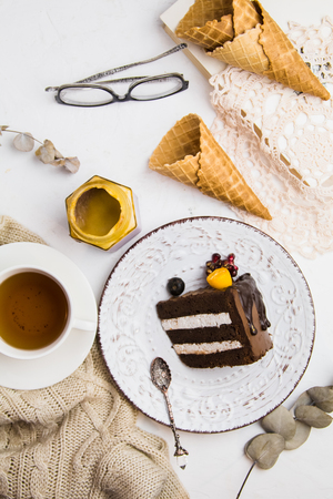 A piece of chocolate cake on a white plate with a Cup of tea, glasses and waffles. Sweet lunch. Good morningの写真素材