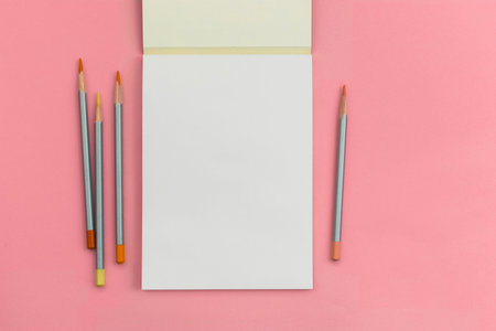 A clean white notebook with a few pencils lies on a beautiful pink background.