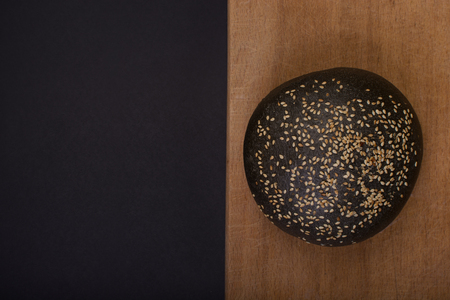 Dark bread made from black dough and sesame lie on wooden desk.の写真素材