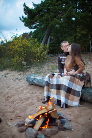 Loving couple sitting on a log by the fire on the rocky beachの写真素材