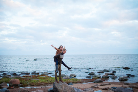 a man wearing a girl on his back on the rocky beachの写真素材