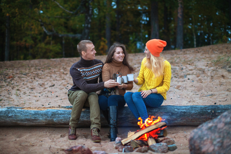 small company communicates sitting on a log by the fire on the beach against the background of the forestの写真素材