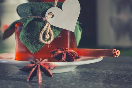 Glass jar with honey covered with green cloth with thread with white paper heart for Valentine's Day. White plate. Star anise star anise, cinnamon sticks.の写真素材