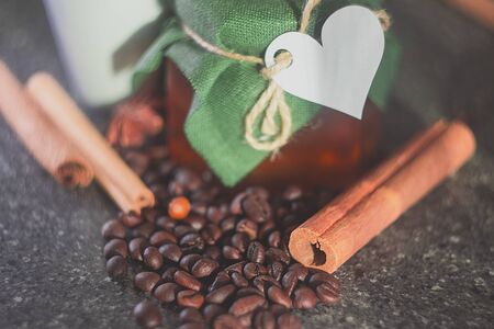 Glass jar with honey covered with green cloth with thread with white paper heart for Valentine's Day. Star anise star anise, cinnamon sticks, coffee grains. White cup.の写真素材