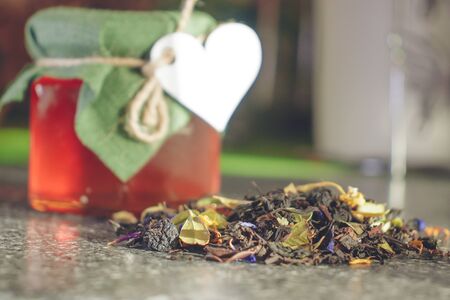 Natural tea brewing of dried berries and leaves of medicinal plants. Glass jar of honey with a lid of natural fabric tied with a thread with a paper heart. Natural products for Valentine's Day.の写真素材