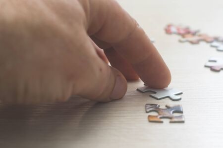 Hard to solve the problem. Collapsible puzzle pieces. Hard to solve the problem. Collapsible puzzle pieces. Puzzle pieces scattered across the table. Hands of a man.の写真素材