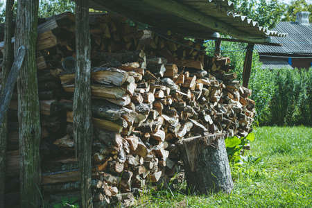 A stack of chopped dry firewood in a village yard. Firewood covered with slate from the rain. Wooden block for chopping firewood.の写真素材