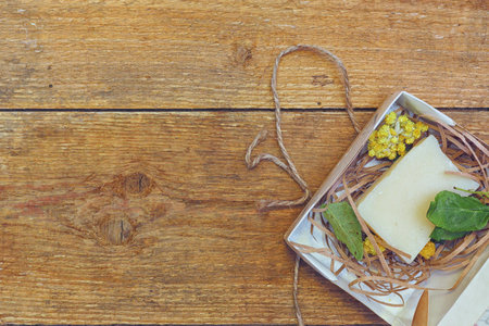 The use of natural products. A handmade piece of fragrant soap on paper chips surrounded by flowers and leaves of medicinal and fragrant plants on aged wooden boards.の写真素材
