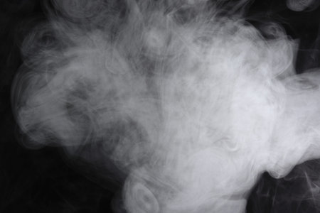 Puffs of white, gray smoke spread on a black background, curling in a fancy dance.