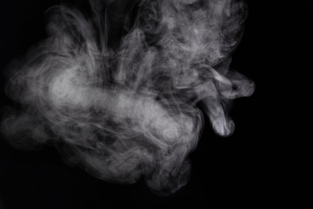 Puffs of white, gray smoke spread on a black background, curling in a fancy dance.