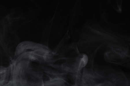 Puffs of white, gray smoke spread on a black background, curling in a fancy dance.の写真素材