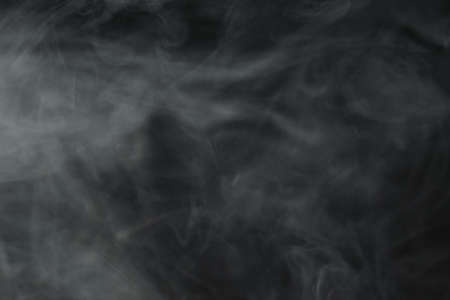 Puffs of white, gray smoke spread on a black background, curling in a fancy dance.の写真素材