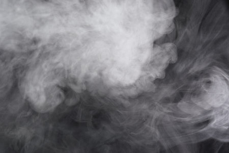 Puffs of white, gray smoke spread on a black background, curling in a fancy dance.
