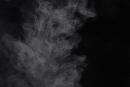 Puffs of white, gray smoke spread on a black background, curling in a fancy dance.