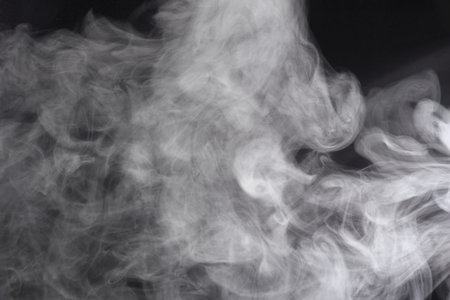 Puffs of white, gray smoke spread on a black background, curling in a fancy dance.