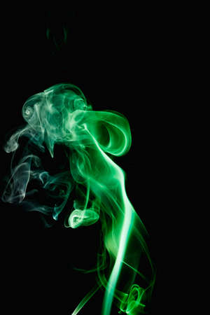Whimsical curls and shapes of green smoke on a dark background. Streaming smoke from a burning incense stick.の写真素材