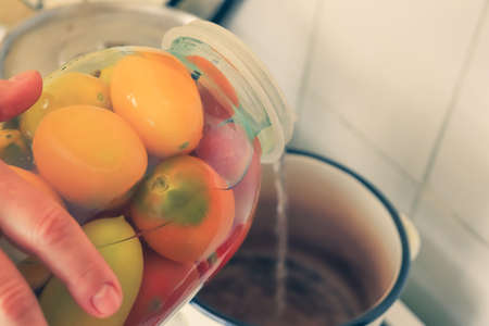 Step by step pickling of tomatoes for the winter in the village. The woman pours the present brine from a jar of tomatoes into a saucepan for further boiling.の写真素材