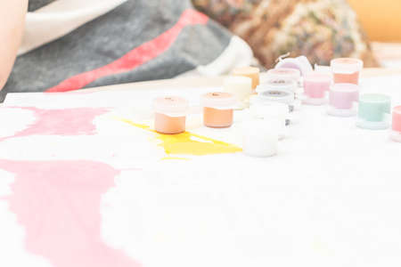 Creative leisure of children. A boy and a girl are sitting on the couch at the table and drawing with paints and felt-tip pens. Children in a high key. Paints in small jars.の写真素材