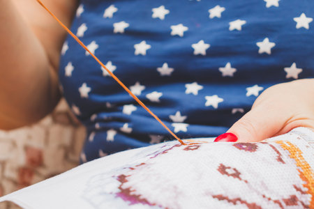 Favorite activity during the pandemic. A woman sitting on a sofa is embroidering with a cross on a...