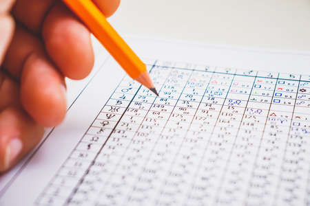 Modern astrologer's desktop. Hand with a pencil. Astrological charts and tables with the coordinates of the planets, astrological symbols close-up.の写真素材