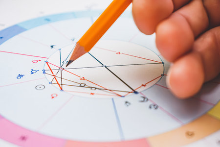 Modern astrologer's desktop. Hand with a pencil. Astrological charts and tables with the coordinates...