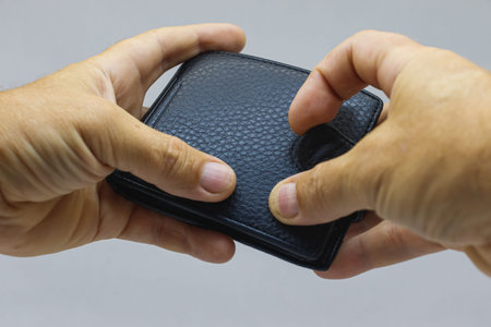 Black leather purse in his hands on a light background close-up. The purse is in the hands of a man.