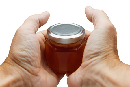 Glass jar with honey in hand close-up. Isolated. A jar in the hands of a man on a white background.