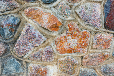 A close-up of the stone wall. The texture of masonry is made of multi-colored stones connected with...