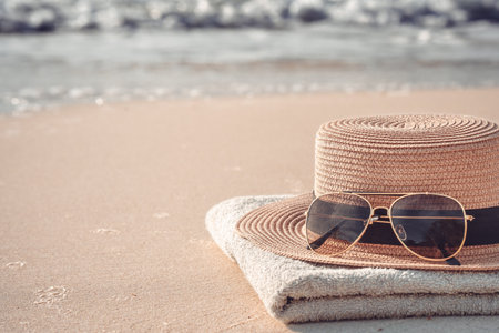 Sunglasses and a hat on the seashore. Close-up of a yellow straw hat and sunglasses on a sandy beach on a tropical coast on a warm sunny day. The concept of summer holidays and vacations.の写真素材