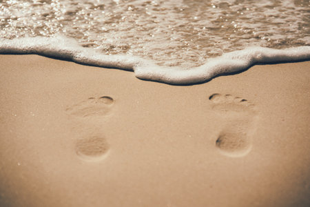 Footprints by the sea, white foam from the sea wave. The concept of vacation in an exotic country, sea bathing and relaxationの写真素材