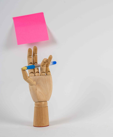 Wooden hand holding pen, pink sticker hanging on white wallの写真素材