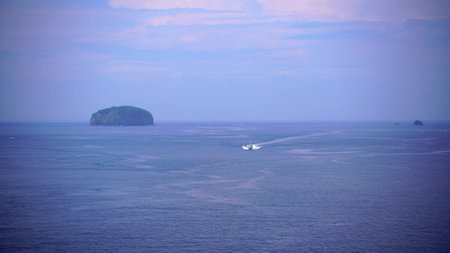 Magnificent seascape. A boat sailing on a deep blue sea with small waves, from the green islands that remained on the horizonの写真素材