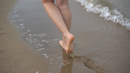 feet on the sand, a man strolling along the beach at dawn during the summer holidays, slow motion, close-up of legs and feet in seawater.の写真素材