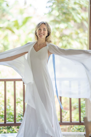 a young woman in a white dress, happy, dancing and singing on a summer veranda, having fun aloneの写真素材