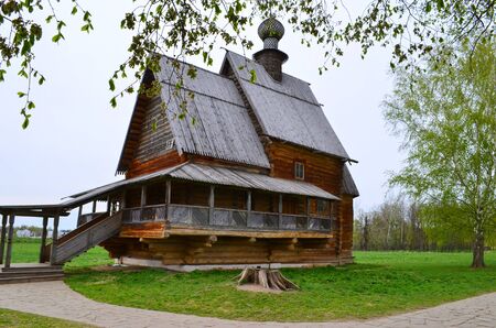 the old wooden house beside the church with birch trees on sky background and green grassの写真素材