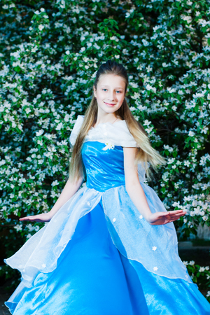 Girl in blue dress on a background of green flowering shrubsの写真素材