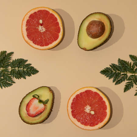 Symmetrically arranged tropical fruit and leaves, with half strawberry on beige background. Minimal flat lay.の写真素材