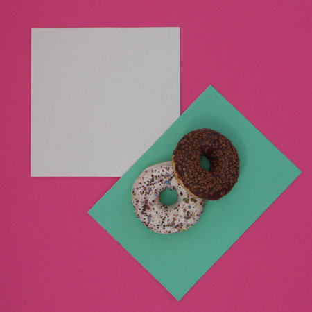 Two donuts sprinkled with chocolate crumbs on a light green surface, with white copy space, all on a pink background. Minimal flat flay scene.の写真素材