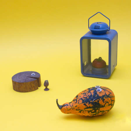 A pumpkin and an old tree with eyes and a strange figure and behind it a blue lantern with red pepper instead of a candle on a yellow background. Minimalistic scene.の写真素材