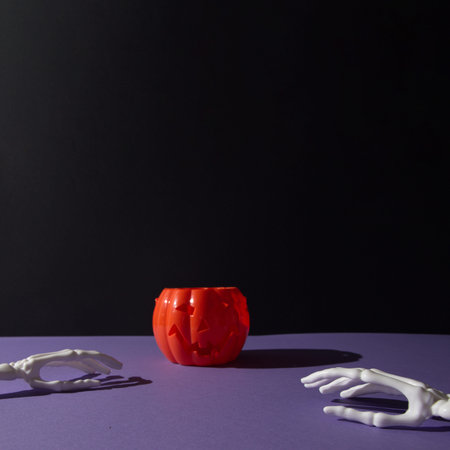 Pumpkin decoration for Helloween and hand bones on purple black background with copy space. Minimal...