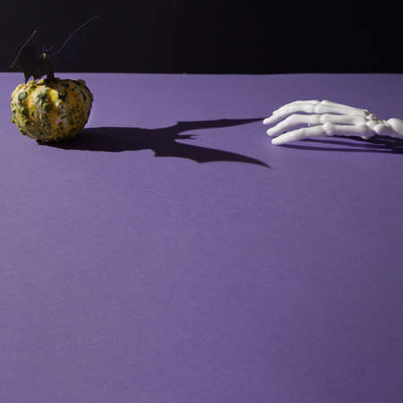 Pumpkins for Halloween and shadow of the bat on a purple background with hand bones with copy space. Minimal scene concept.の写真素材