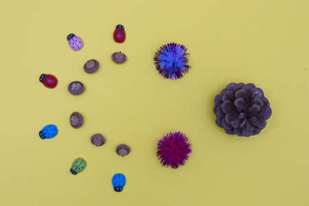 A cone against colorful ladybugs and acorns arranged in a semicircle on a yellow background. Flat lay minimalistic composition.の写真素材
