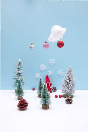 A girl in red in a pine forest on the snow with a cloud from which New Year's decorations are falling. Cones scattered on the snow. Minimalistic look.の写真素材