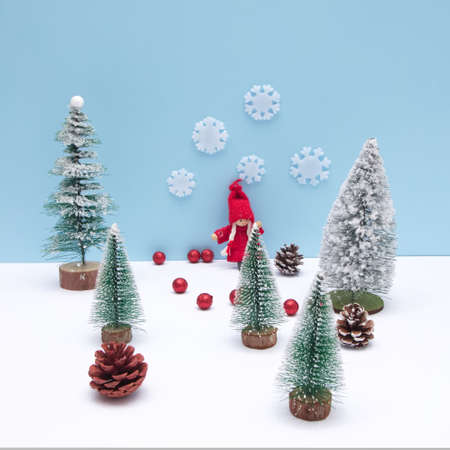 A girl in red in a pine forest on the snow with a blue background. Cones scattered on the snow. Minimalistic look.の写真素材