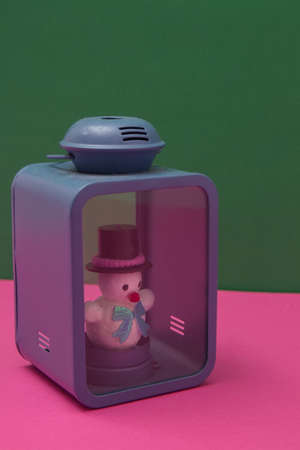 Snowman instead of a candle in a blue lantern on a pink green background. Minimal composition.の写真素材